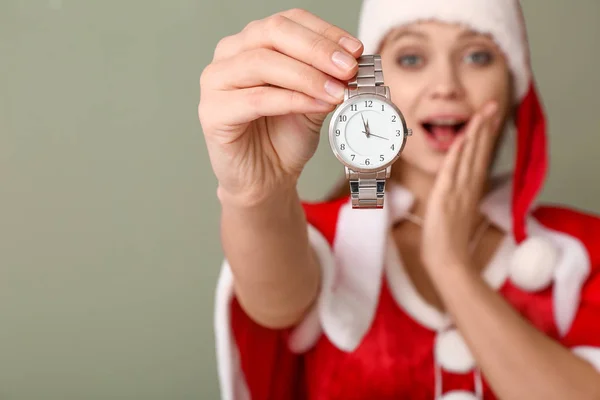 Έκπληκτη νεαρή γυναίκα με κοστούμι Σάντα και με ρολόι στο φόντο χρώμα. Χριστούγεννα αντίστροφη μέτρηση έννοια — Φωτογραφία Αρχείου