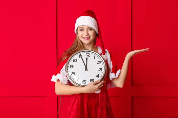 Νεαρή γυναίκα με κοστούμι Σάντα και με ρολόι στο φόντο χρώμα. Χριστούγεννα αντίστροφη μέτρηση έννοια — Φωτογραφία Αρχείου