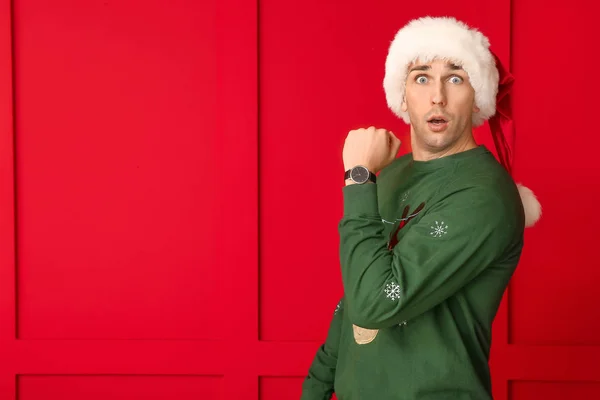 Surprised young man in Santa hat and with watch on color background. Christmas countdown concept — Stock Photo, Image