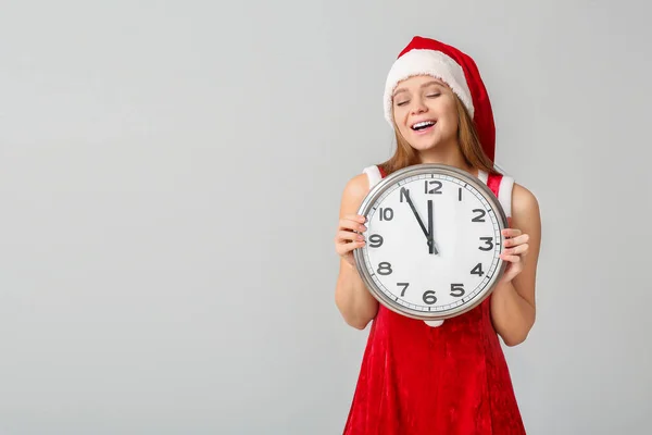 Ung kvinna i Santa kostym och med klocka på ljus bakgrund. Julnedräkning koncept — Stockfoto