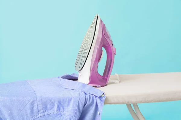 Bügeleisen und saubere Kleidung an Bord vor farbigem Hintergrund — Stockfoto