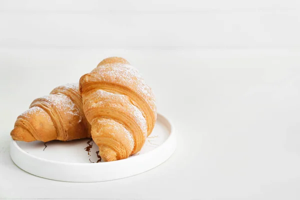 Assiette avec de savoureux croissants sur table blanche — Photo