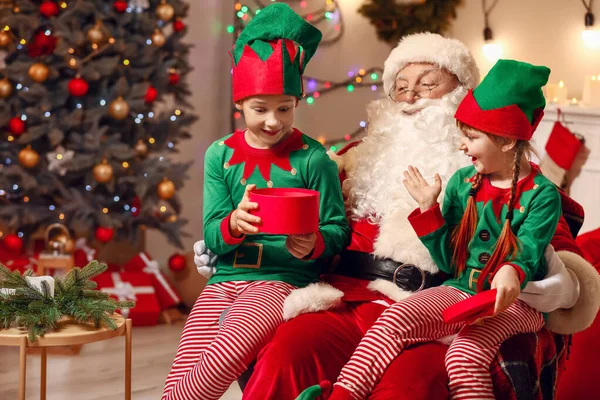 Weihnachtsmann und kleine Wichtelkinder öffnen Geschenk in weihnachtlich dekoriertem Raum — Stockfoto