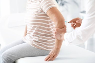 Doktor klinikte eklem ağrısı olan olgun bir kadına eklem iğnesi yapıyor.