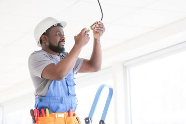 Afrika kökenli Amerikalı elektrikçi odada elektrik tesisatı yapıyor.