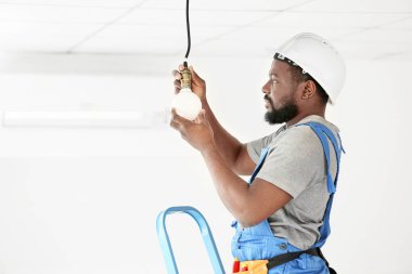Afrika kökenli Amerikalı elektrikçi odada elektrik tesisatı yapıyor.