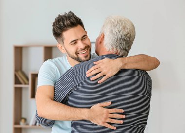 Young man and his father hugging at home clipart
