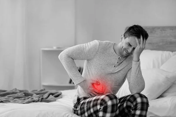 Young man suffering from abdominal pain in bedroom — Stock Photo, Image