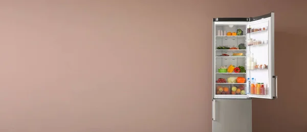 Open fridge full of food on color background with space for text — Stock Photo, Image