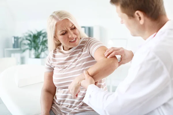 Doctor examining mature woman with joint pain in clinic — Stock Photo, Image