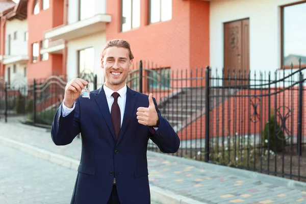 Männlicher Immobilienmakler mit Schlüssel zeigt Daumen-hoch-Geste im Freien — Stockfoto