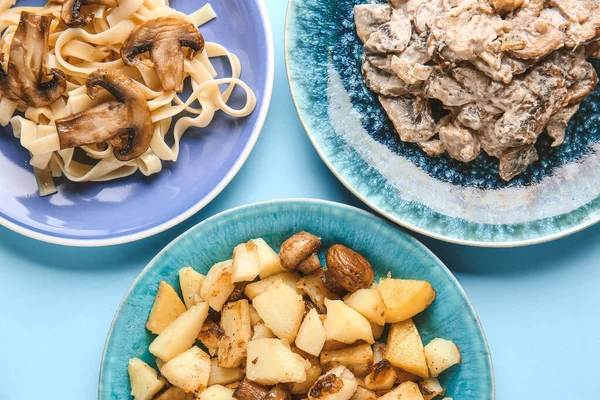 Plates with different mushrooms dishes on color background