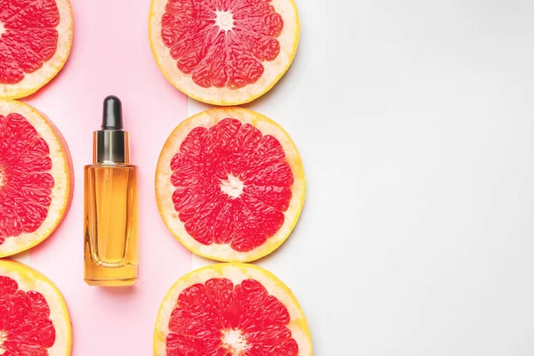 Lahvička esenciálního oleje a grapefruitové plátky na barevném pozadí — Stock fotografie