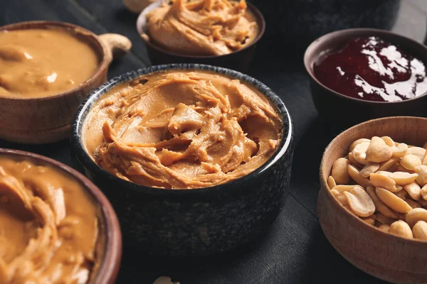 Cuencos con sabrosa mantequilla de maní y mermelada en la mesa oscura — Foto de Stock