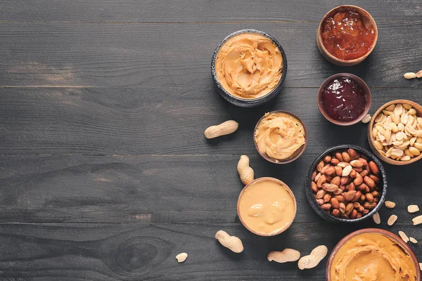 Tigelas com manteiga de amendoim saborosa e geléia na mesa escura — Fotografia de Stock