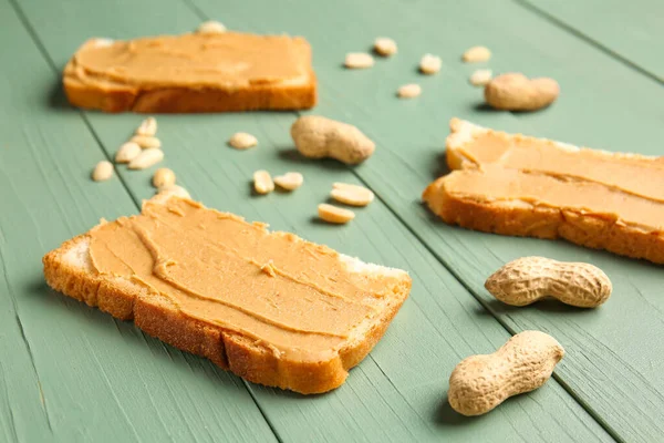 Plátky chleba s chutným arašídovým máslem na barevném dřevěném pozadí — Stock fotografie