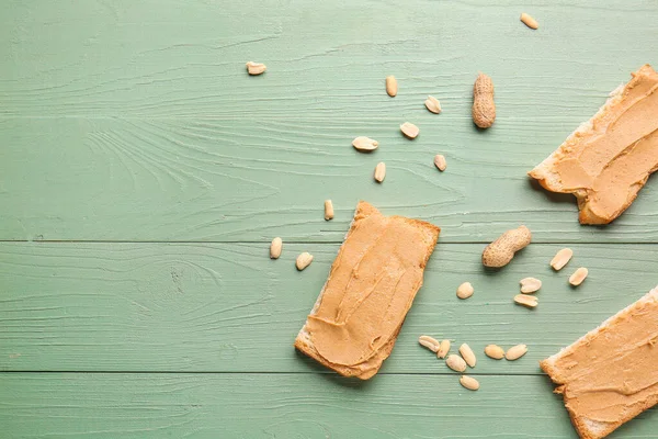 Slices of bread with tasty peanut butter on color wooden background — Stock Photo, Image