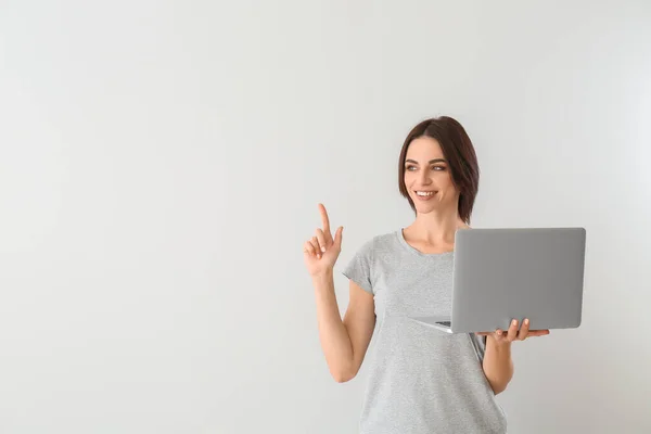 Schöne junge Frau mit Laptop und erhobenem Zeigefinger auf grauem Hintergrund — Stockfoto