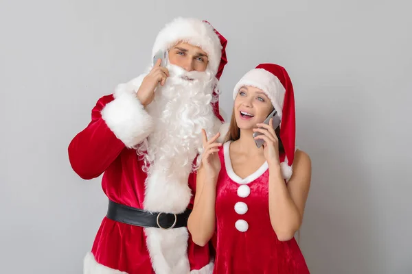 Pareja joven vestida de Santa Claus con teléfonos móviles sobre fondo claro — Foto de Stock