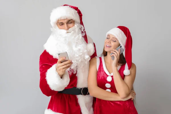 Young couple dressed as Santa with mobile phones on light background — Stock Photo, Image