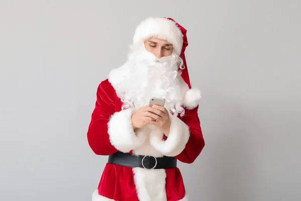 Young man in Santa costume and with mobile phone on light background — Stock Photo, Image