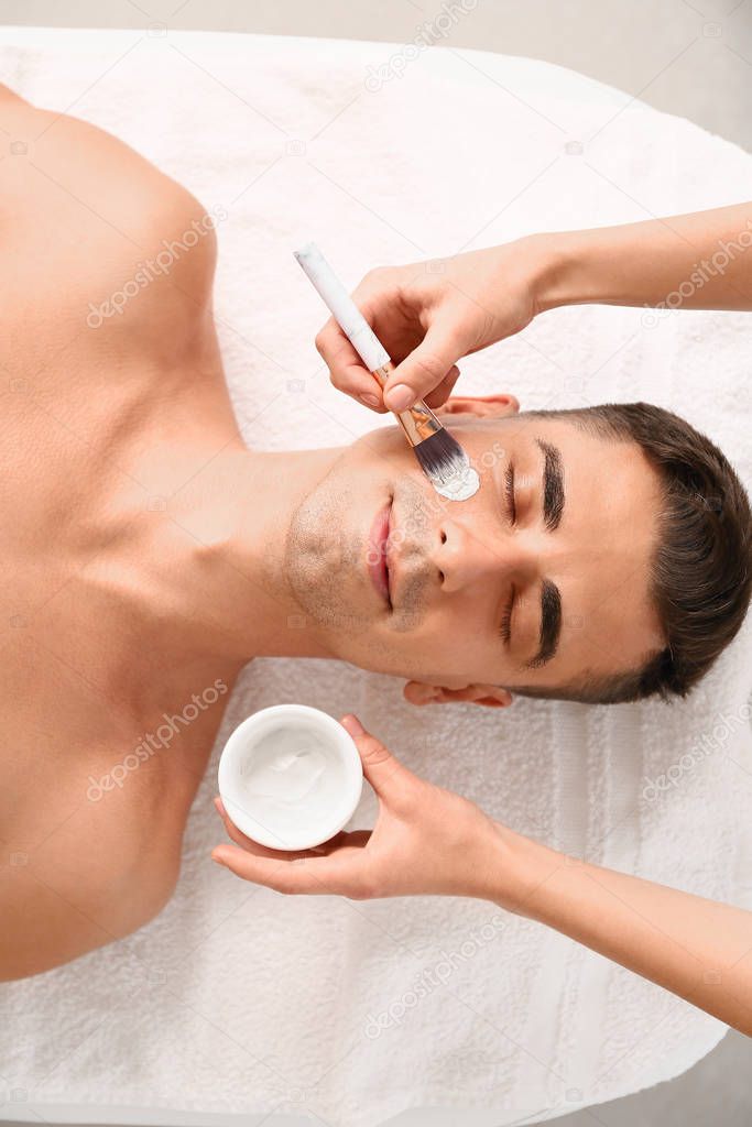 Handsome man undergoing treatment with facial mask in beauty salon