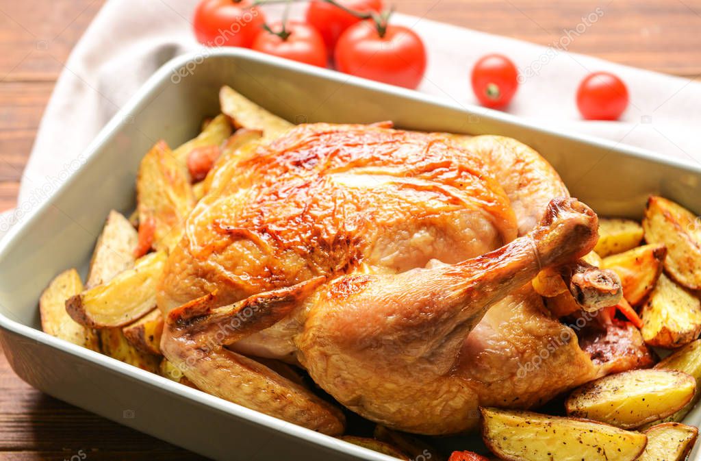 Dish with baked chicken and potato on wooden table