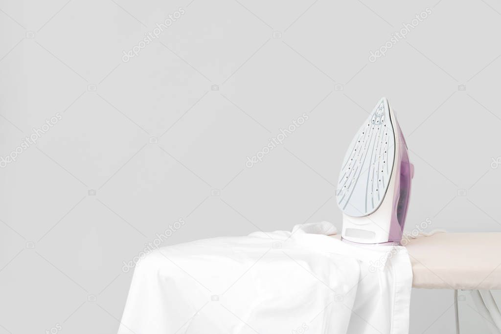 Iron and clean clothes on board against grey background