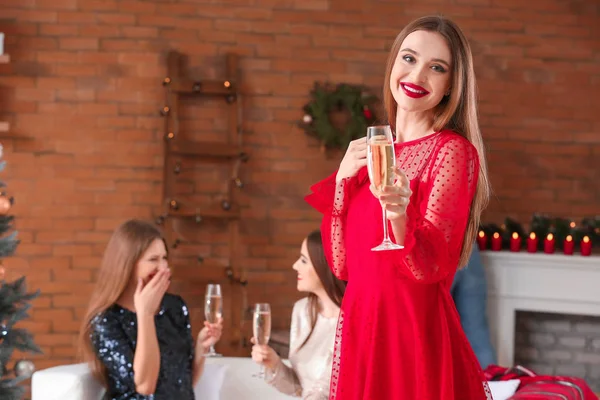 Beautiful young woman with champagne and her friends celebrating Christmas at home — Stock Photo, Image