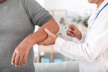 Doktor evde eklem ağrısı olan olgun bir adama yakın çekim yapıyor.
