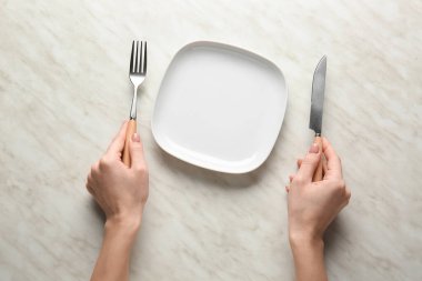 Masasında boş tabak ve çatal bıçak takımı olan bir kadın.