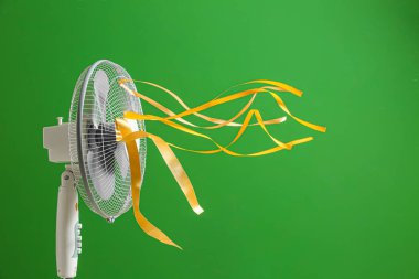 Electric fan with fluttering ribbons on color background clipart