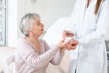 Parkinson sendromlu yaşlı bir kadına klinikte su içiren kadın doktor.