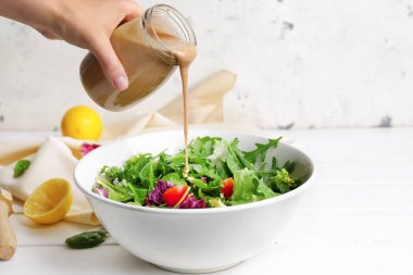 Kadın kavanozdan sebze salatasına lezzetli tahini dolduruyor.
