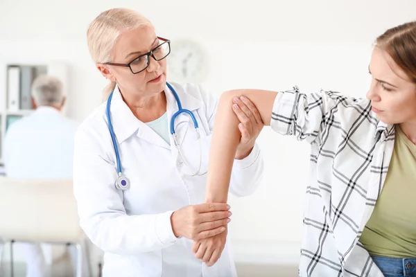 Зрелый врач осматривает молодую женщину с болью в суставах в клинике — стоковое фото