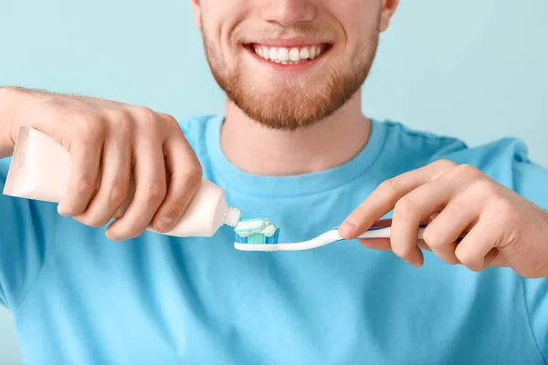 Young man with toothbrush and paste on color background — Stock Photo, Image