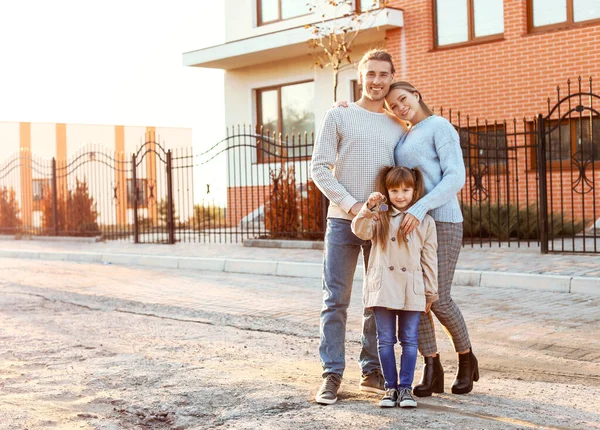 Família jovem com chave perto de sua nova casa — Fotografia de Stock