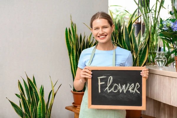 Retrato de florista feminina segurando quadro com palavra FLORES na loja — Fotografia de Stock