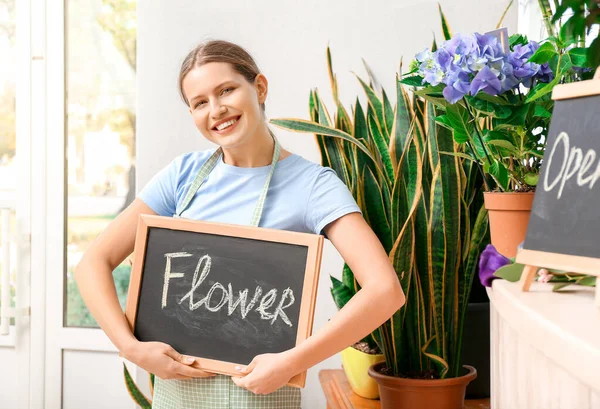 Retrato de florista feminina segurando quadro com palavra FLORES na loja — Fotografia de Stock