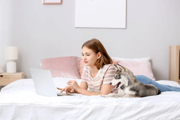 Cute teenage girl with funny husky puppy and laptop on bed at home — Stock Photo, Image