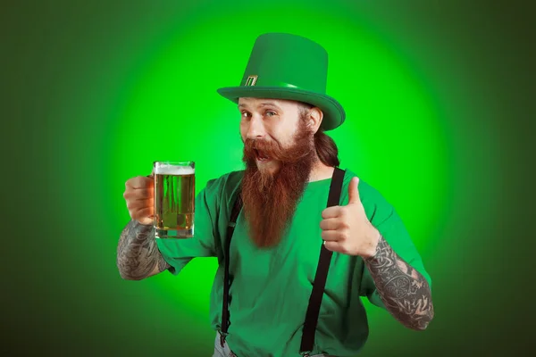 Homem barbudo com copo de cerveja mostrando gesto de polegar para cima no fundo escuro. Celebração do Dia de São Patrício — Fotografia de Stock