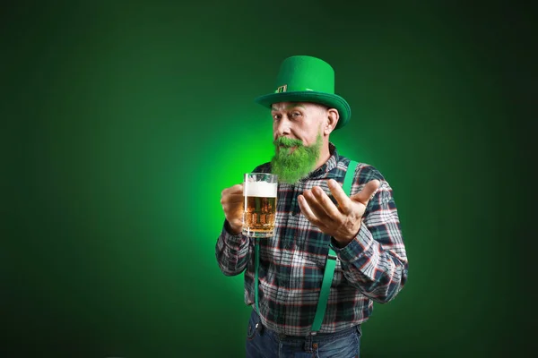 맥주 한 잔을 들고 어두운 배경에 있는 시청자들을 초대하는 웃기는 성숙 한 남자. 성 패트릭의 날 기념행사 — 스톡 사진