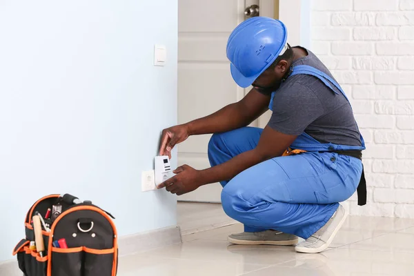 African-American electrician using socket voltage regulator in room — Stock Photo, Image