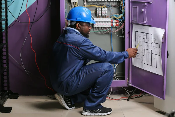 Eletricista afro-americano realizando fiação no quadro de distribuição — Fotografia de Stock