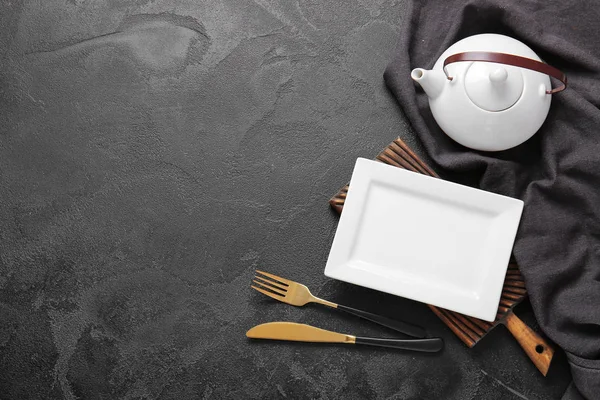 Empty plate, teapot and cutlery on dark background — Stock Photo, Image