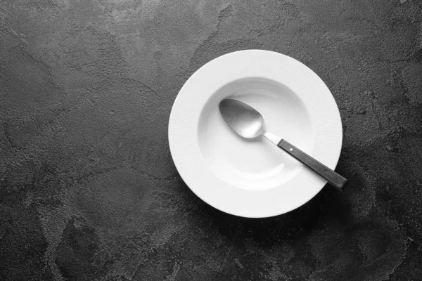 Пустая тарелка и ложка на темном фоне — стоковое фото