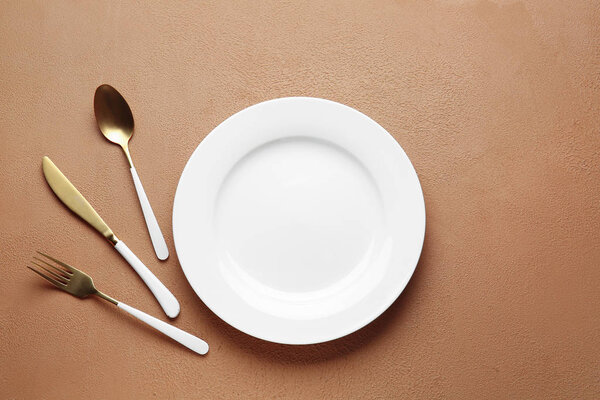 Empty plate and cutlery on color background