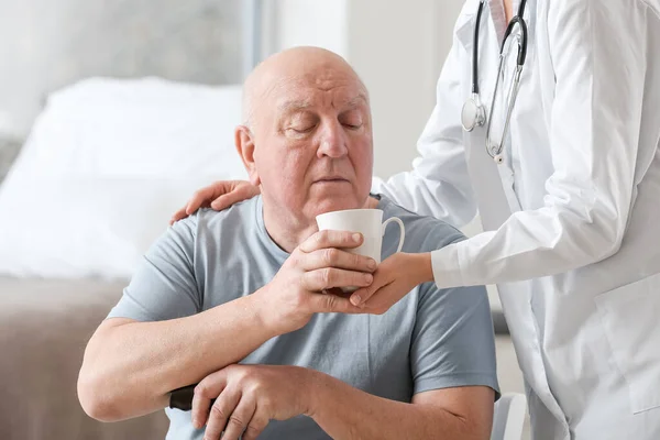 Жінка-лікар дає старшому чоловікові, який страждає від синдрому Паркінсона чашку чаю в клініці — стокове фото