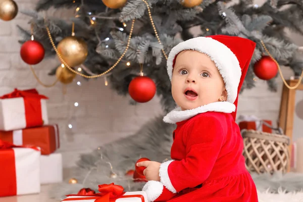 Schattig klein baby in Santa Claus kostuum en met kerstcadeau thuis — Stockfoto