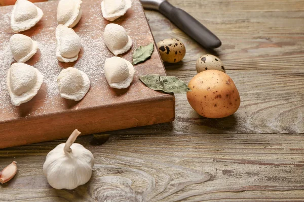 Board with raw dumplings and ingredients on wooden background — Stock Photo, Image